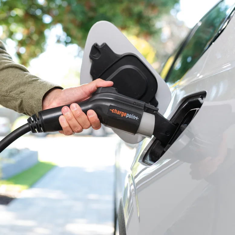 Hand plugging a ChargePoint J1772 connector into an EV charge port outdoors
