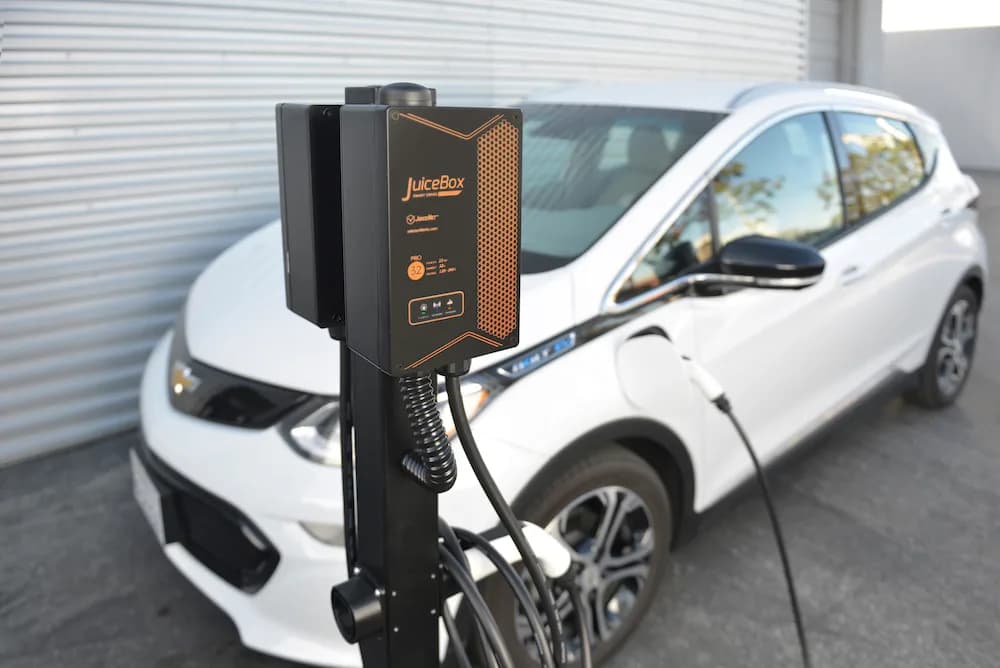 Pedestal-mounted JuiceBox charger plugged into a white electric car