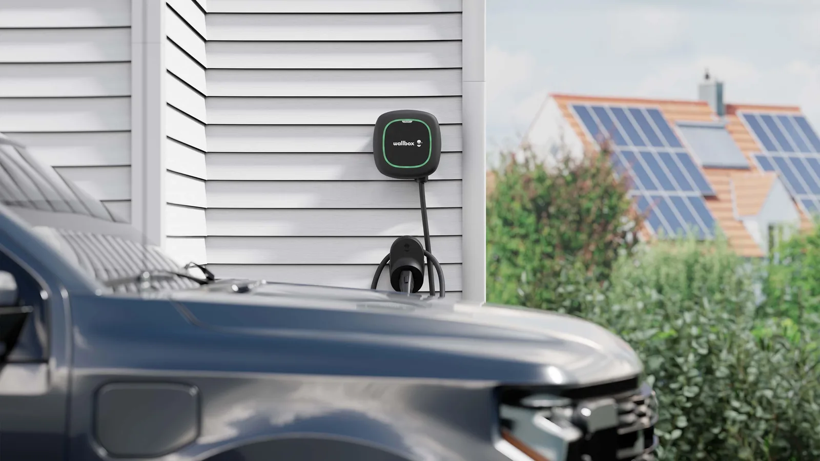 Wallbox Pulsar Plus mounted on white siding, charging an electric pickup outside a solar-equipped home